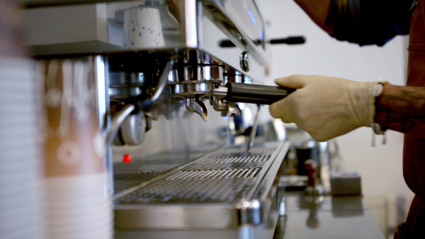 Unrecognizable man barista working with gloves in coffee shop, making coffee.