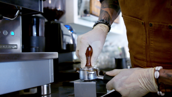 Unrecognizable man barista working with gloves in coffee shop, making coffee.