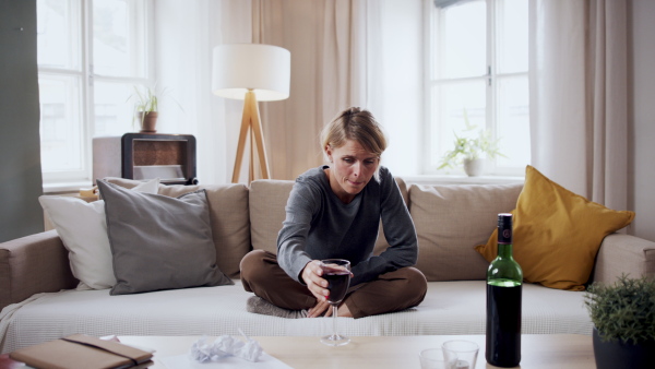 Depressed woman with wine indoors at home, mental health and alcohol addiction concept.