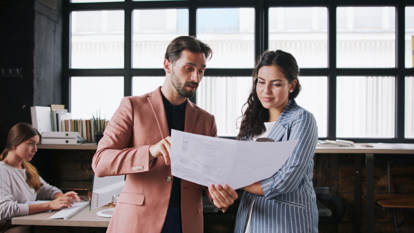 Front view portrait of young businesspeople working indoors in office, discussing blueprints.