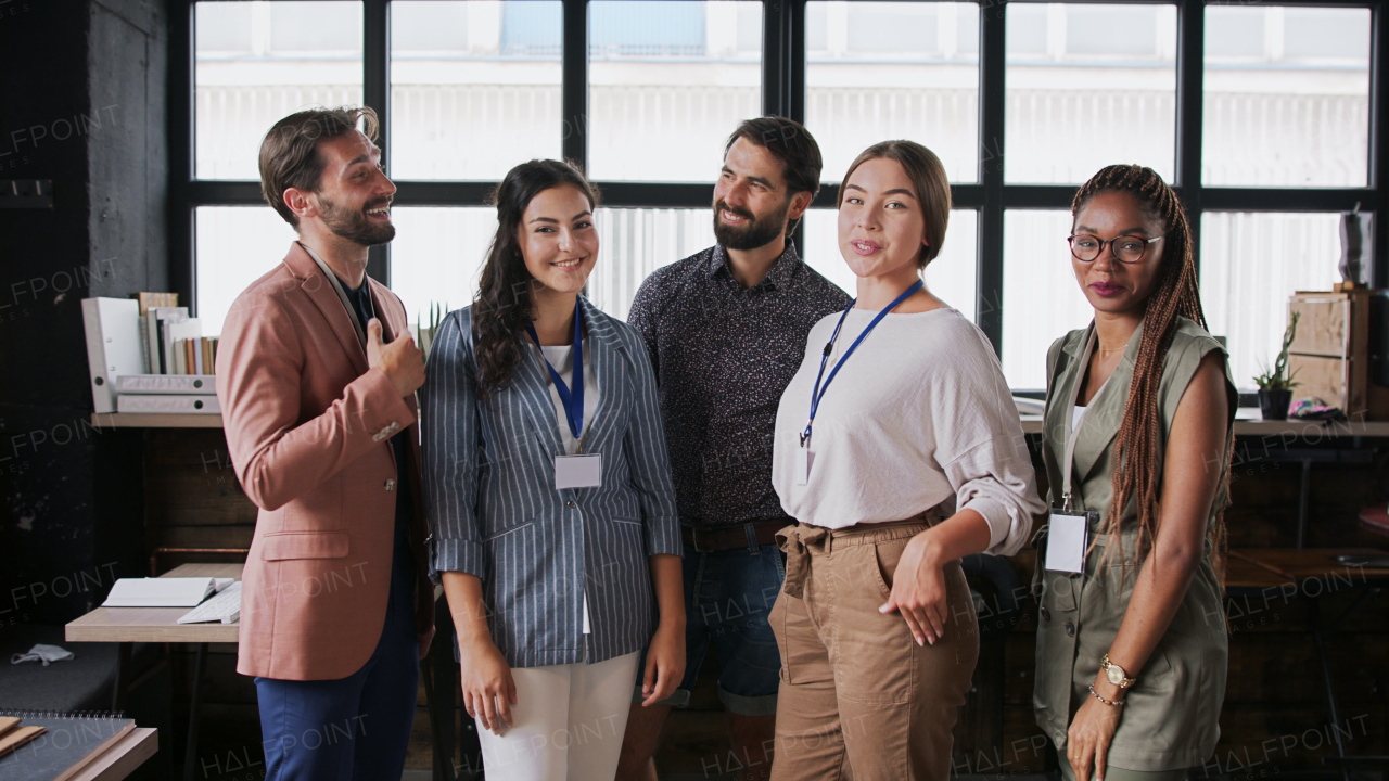 Front view portrait of young businesspeople standing indoors in office, looking at camera.