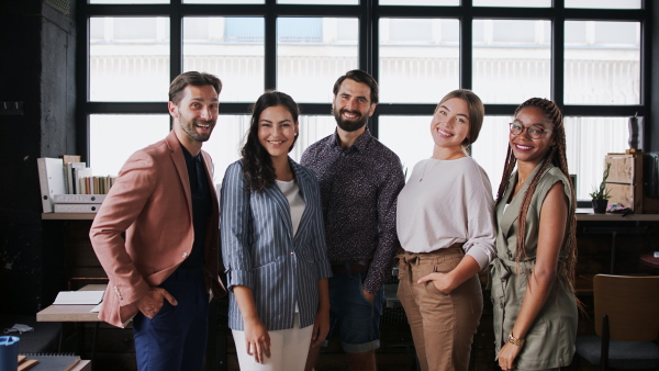 Front view portrait of young businesspeople standing indoors in office, looking at camera.