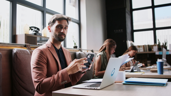 Portrait of group of young businesspeople with laptop sitting and working indoors in office.