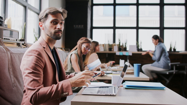 Portrait of group of young businesspeople with laptop sitting and working indoors in office.