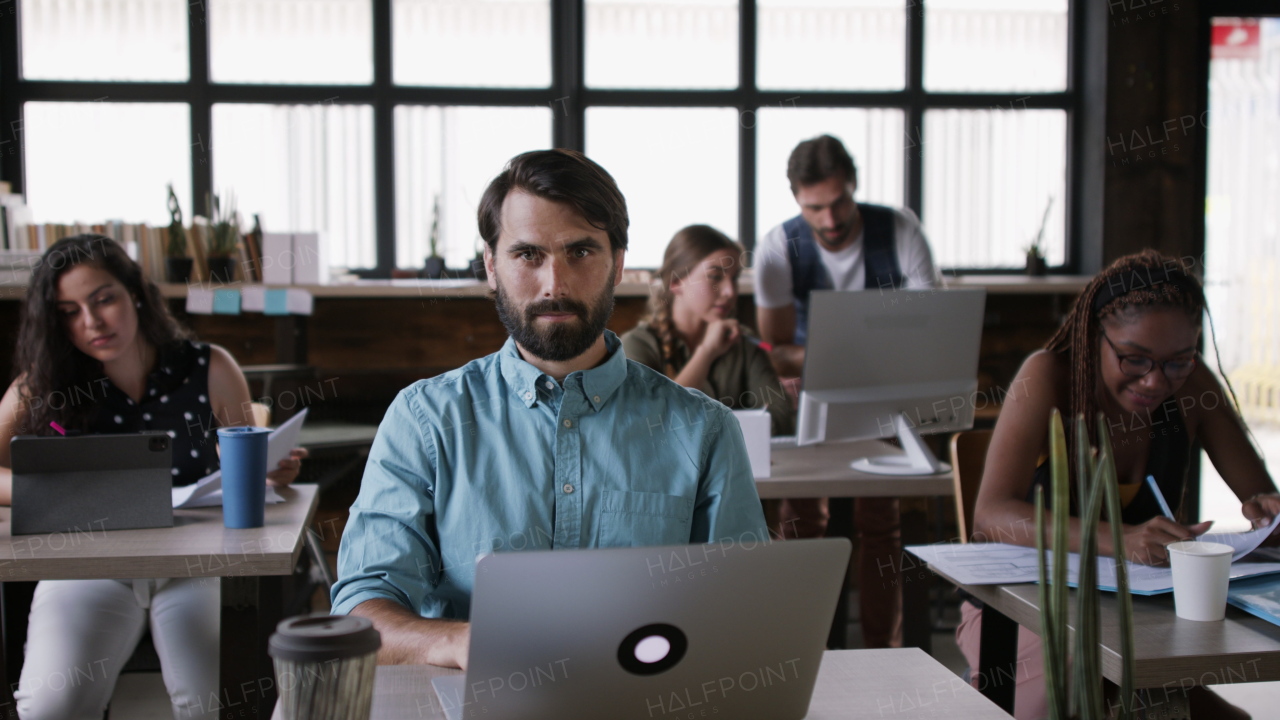 Portrait of group of young businesspeople with laptop sitting and working indoors in office.