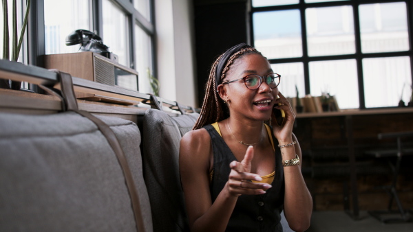 Portrait of young african-american businesswoman indoors in office, using smartphone.