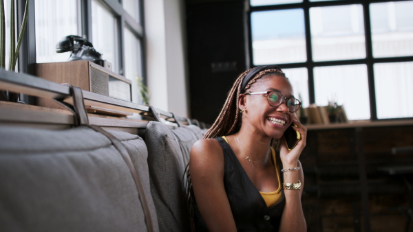 Portrait of young african-american businesswoman indoors in office, using smartphone.