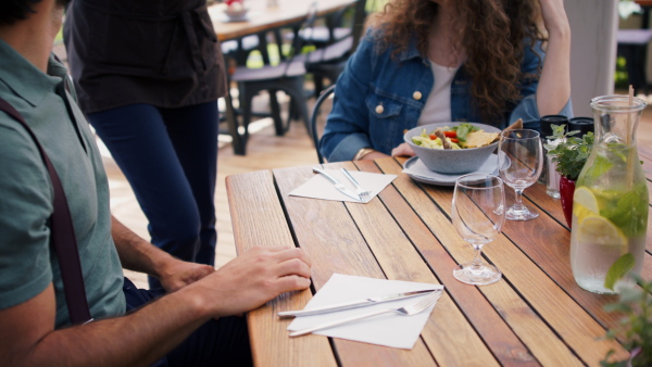 Unrecognizable waitress with face mask serving happy couple outdoors on terrace restaurant.