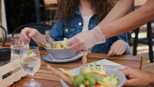 Midsection of waitress with gloves serving lunch to couple outdoors on terrace restaurant.