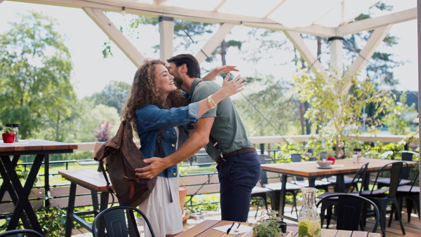 Happy young couple greeting outdoors on terrace restaurant, hugging.