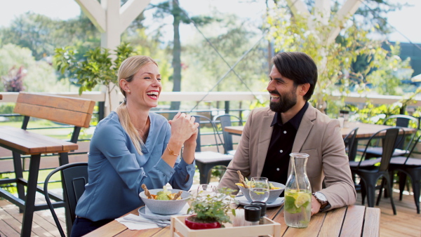 Happy couple sitting at the table outdoors on terrace restaurant, talking.