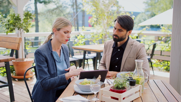 Man and woman business partners with tablet sitting outdoors on terrace restaurant, discusssing issues.