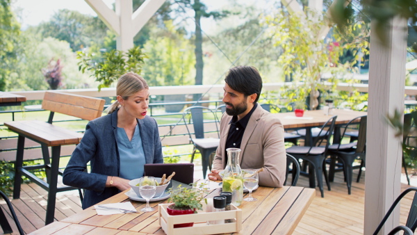 Man and woman business partners with tablet sitting outdoors on terrace restaurant, discusssing issues.