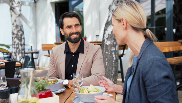 Happy couple sitting at the table outdoors on terrace restaurant, talking.