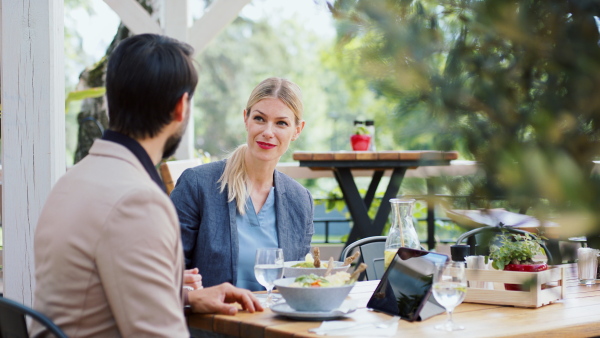 Man and woman business partners with tablet sitting outdoors on terrace restaurant, discusssing issues.