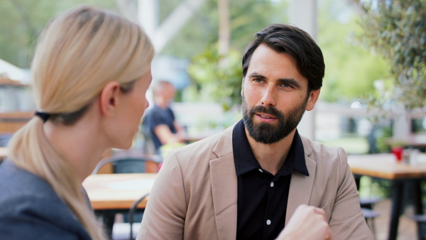 Man and woman business partners sitting outdoors on terrace restaurant, discusssing issues.