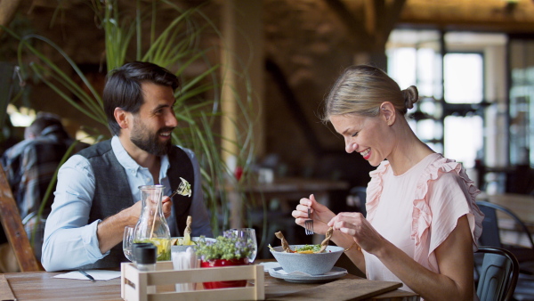 Happy couple sitting indoors in restaurant, talking when having lunch.