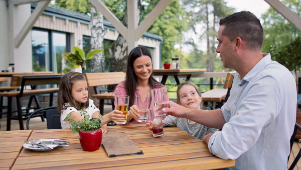 Happy family with children outdoors on terrace restaurant, clinking glasses.