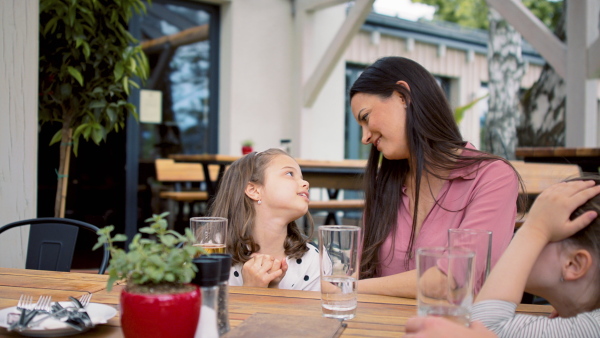 Young mother with small daughters outdoors on terrace restaurant, talking.