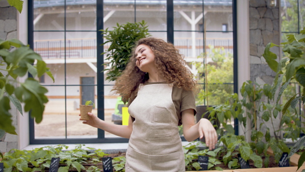 Portrait of cheerful woman gardener dancing in greenhouse, holding plant.