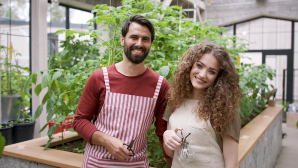 Portrait of man and woman gardener with apron standing in greenhouse, looking at camera.