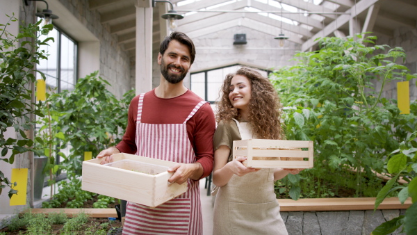 Front view portrait of man and woman gardeners standing in greenhouse, looking at camera.