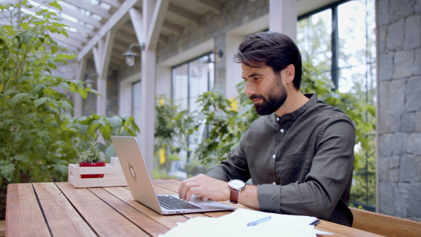 Portrait of young man with laptop sitting indoors in green office, working.