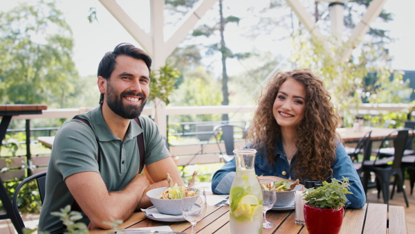 Happy couple sitting at the table outdoors on terrace restaurant, looking at camera.