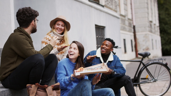 Group of cheerful young people outdoors in town, eating pizza. Coronavirus concept.