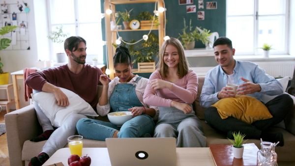 A group of young flatmates sitting on sofa and watching movie, house sharing concept.