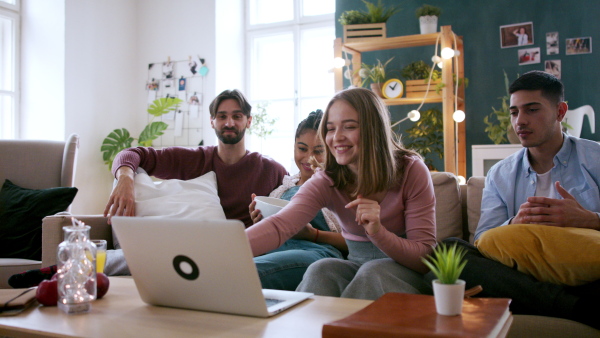 A group of young flatmates sitting on sofa and watching movie, house sharing concept.