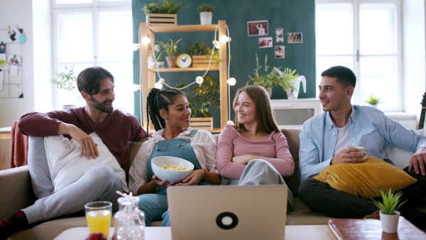 A group of young flatmates sitting on sofa and watching movie, house sharing concept.