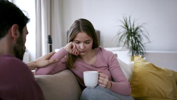 Sad young woman talking to male friend on sofa, house sharing concept.