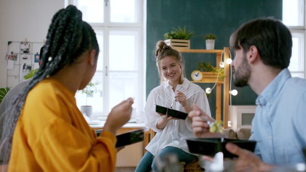 Group of cheerful friends eating take away food indoors, food delivery and house sharing concept.