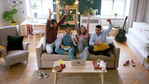 A group of excited young flatmates sitting on sofa and watching movie, house sharing concept.