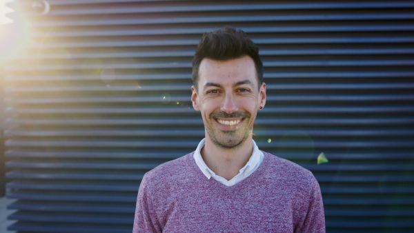 Portrait of young man standing outdoors against dark background, looking at camera and laughing.