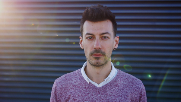 Portrait of young man standing outdoors against dark background, looking at camera.