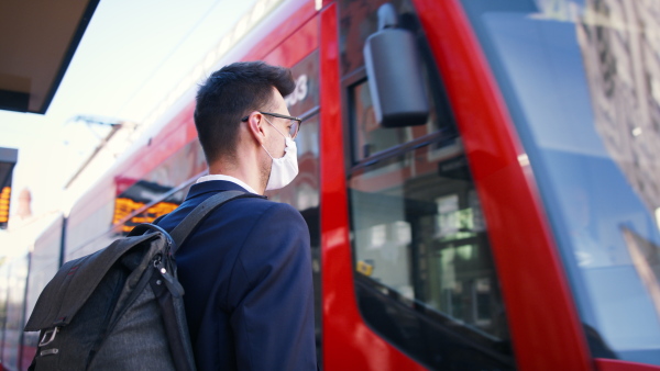 Young commuter with face mask standing outdoors on bus stop, travelling to work.