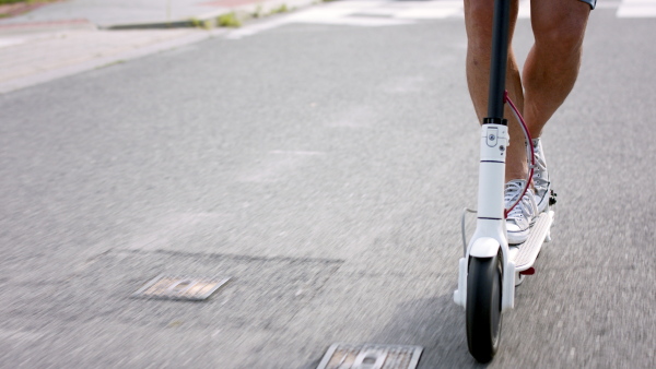 Midsection of unrecognizable commuter riding electric scooter outdoors in city, ecologic transport concept.