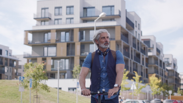 Mature man commuter with electric scooter outdoors in city, going to work. Copy space.