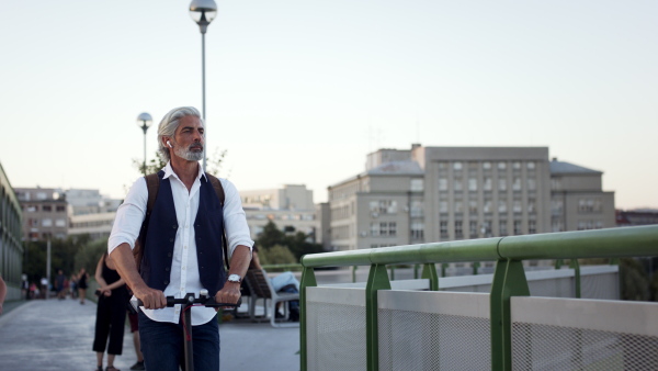 Mature man commuter with electric scooter outdoors in city, going to work. Copy space.