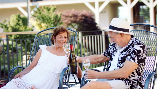 Senior couple on sunbeds outdoors on holiday, drinking wine and talking.