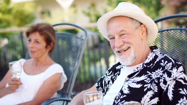 Senior couple on sunbeds outdoors on holiday, drinking wine and talking.