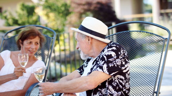 Happy senior couple with wine outdoors on holiday, clinking glasses.