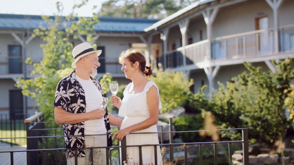 A senior couple holding wine outdoors on holiday, talking.