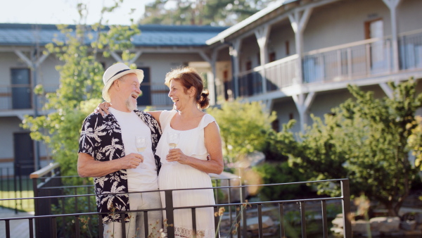 A senior couple holding wine outdoors on holiday, laughing.