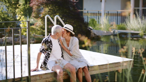 Affectionate senior couple resting outdoors on holiday, sitting and kissing.