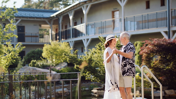 Happy senior couple by hotel outdoors on holiday, dancing.