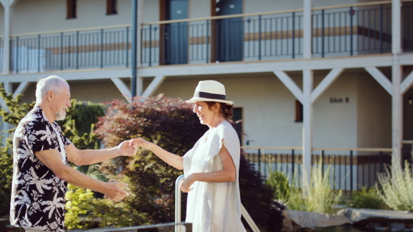 Happy senior couple by hotel outdoors on holiday, dancing.