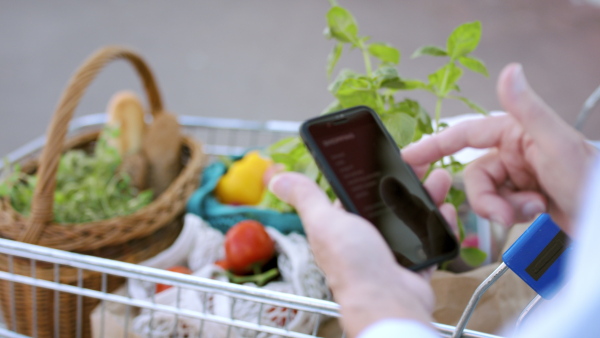 Hands of unrecognizable senior with smartphone doing shopping in supermarket, checking.